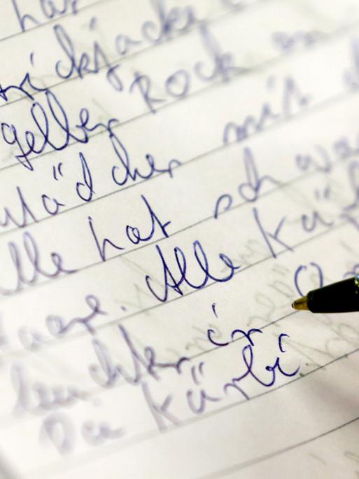 Eine weibliche Hand mit Kugelschreiber schreibt in der Volkshochschule Rostock bei einem Analphabten-Grundkurs in ein Heft.