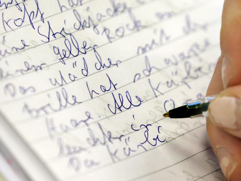 Eine weibliche Hand mit Kugelschreiber schreibt in der Volkshochschule Rostock bei einem Analphabten-Grundkurs in ein Heft.