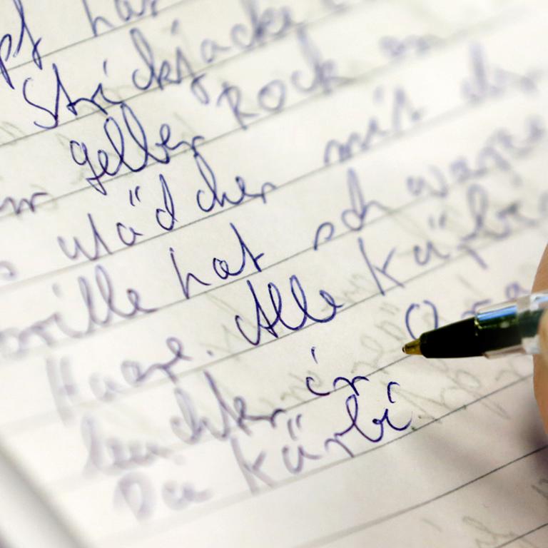 Eine weibliche Hand mit Kugelschreiber schreibt in der Volkshochschule Rostock bei einem Analphabten-Grundkurs in ein Heft.