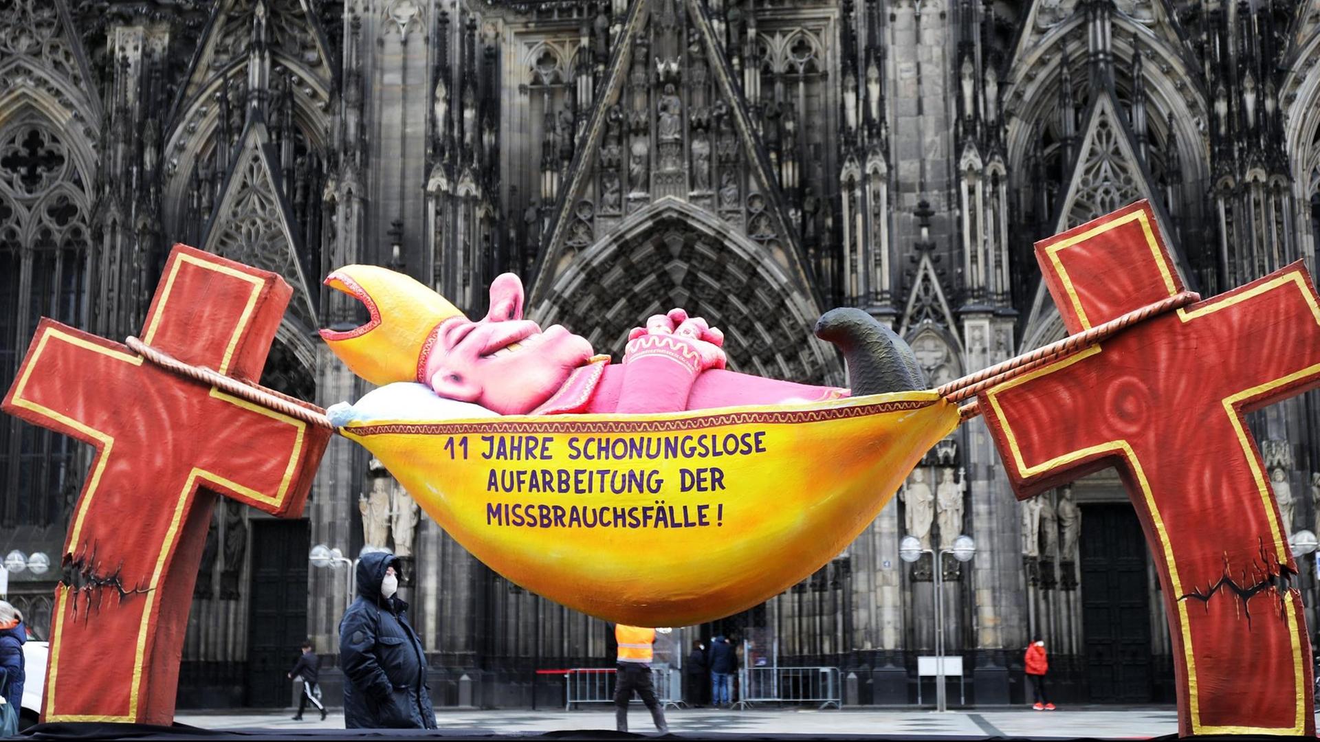 Die Plastik des Künstlers Jacques Tilly mit dem Slogan "11 Jahre schonungslose Aufarbeitung der Missbrauchsfälle!" steht vor dem Kölner Dom