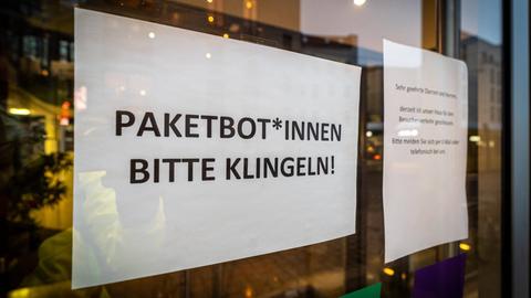 Ein Papier hinter einem Fenster, auf dem steht: "Paketbot*Innen Bitte Klingeln!"