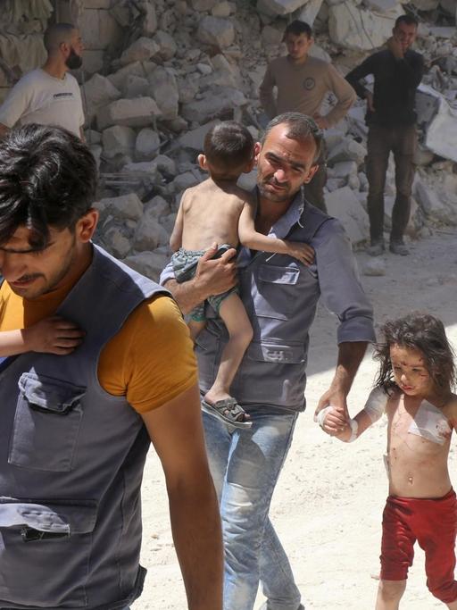 Syrische Männer tragen weinende Kinder zwischen den Trümmern der zerstörten Stadt Aleppo in Syrien.