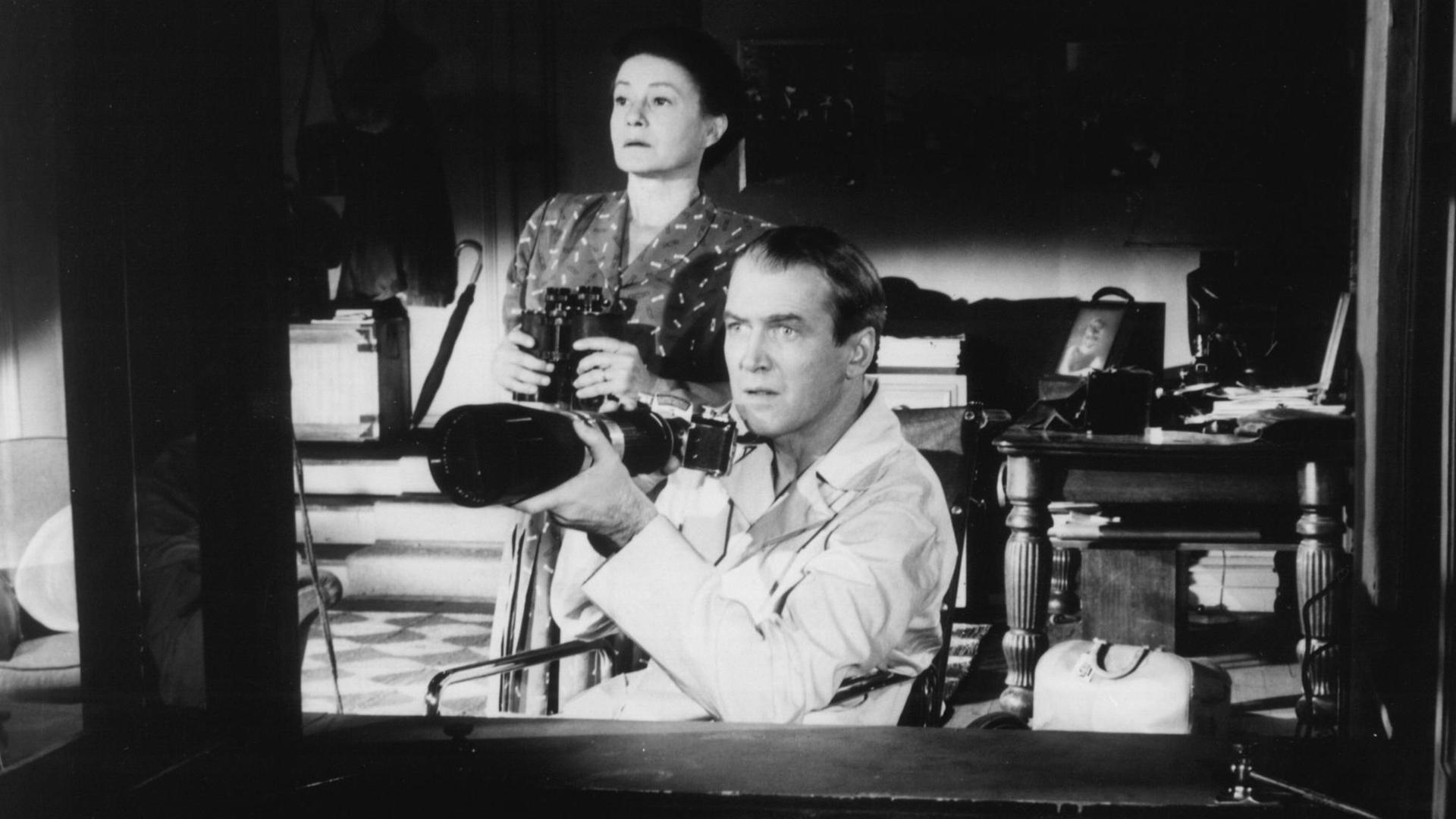 Szene aus "Das Fenster zum Hof": Ein Mann mit Teleobjektiv, im Rollstuhl sitzend und eine Frau schauen aus einem Fenster.