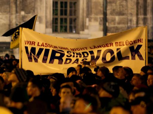 Pegida-Demonstranten halten ein Tranparent hoch, auf dem "Wir sind das Volk" steht.
