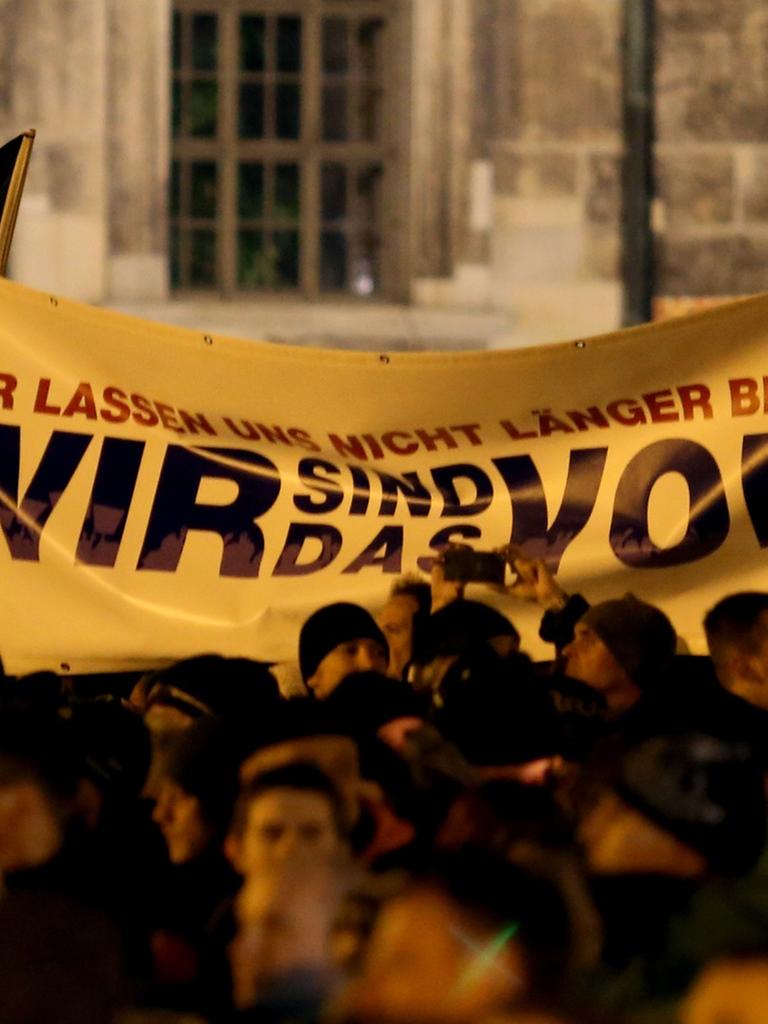Pegida-Demonstranten halten ein Tranparent hoch, auf dem "Wir sind das Volk" steht.