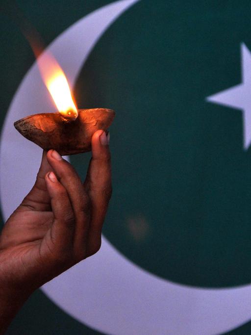 Eine Kinderhand hält eine Lampe vor der pakistanischen Flagge.