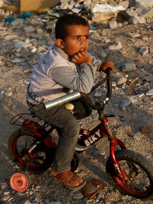 Ein Junge sitzt auf seinem Fahrrad im Gazastreifen inmitten von zerstörten Gebäuden.