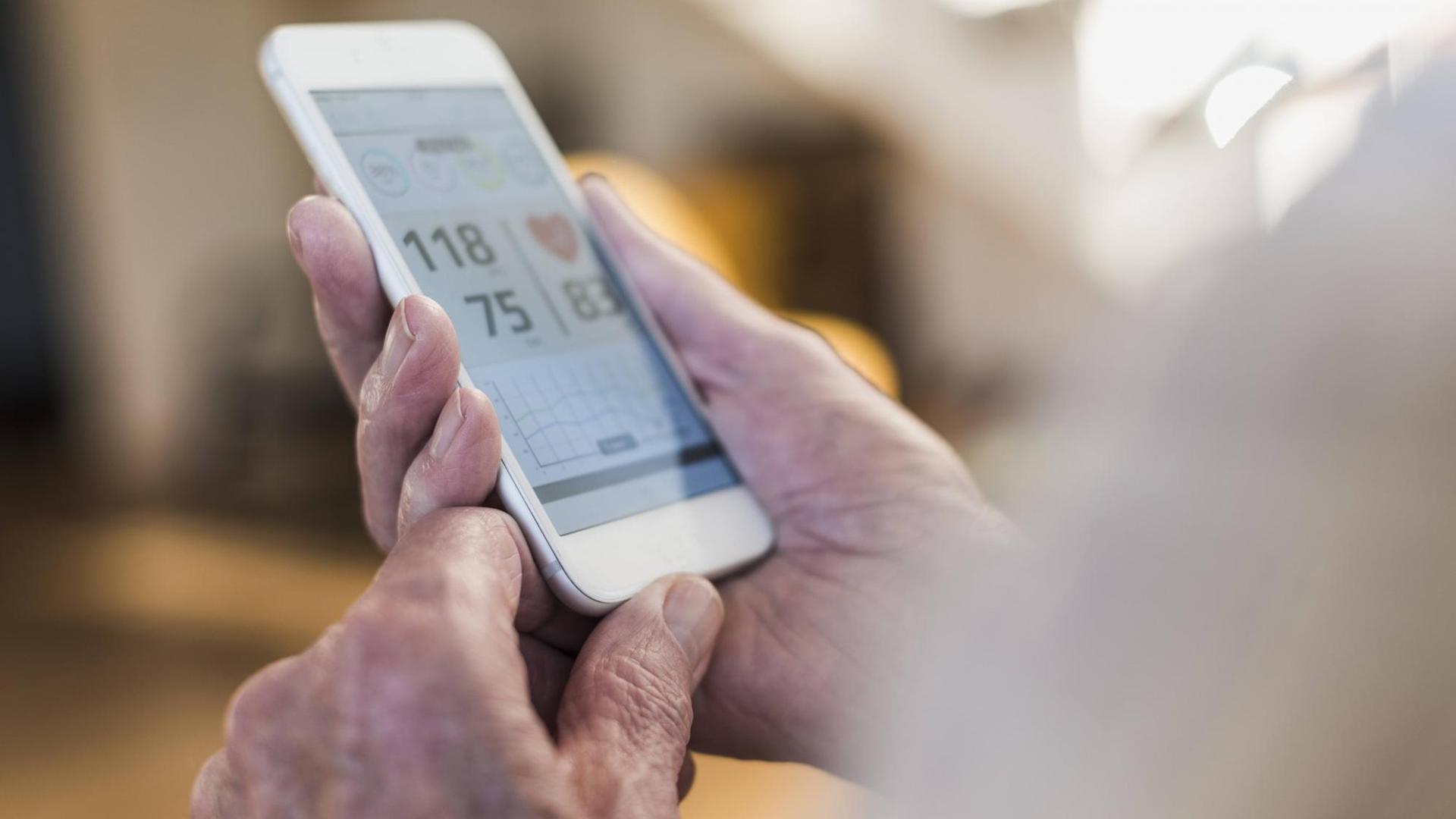 Älterer Mann schaut auf sein Smartpone, das Blutdruckwerte anzeigt.
