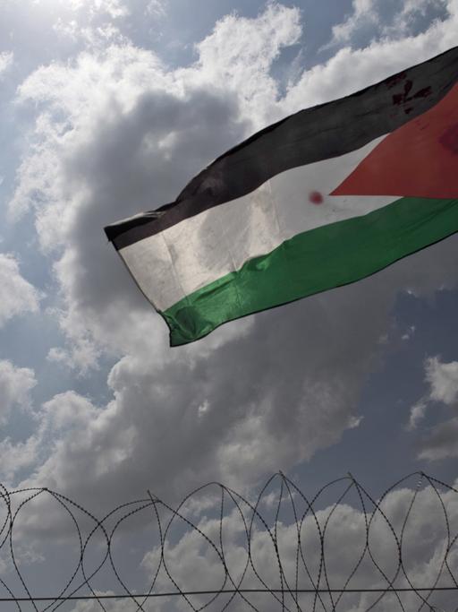 Ein junger Palästinenser schwenkt auf der Grenzbefestigung die Fahne.