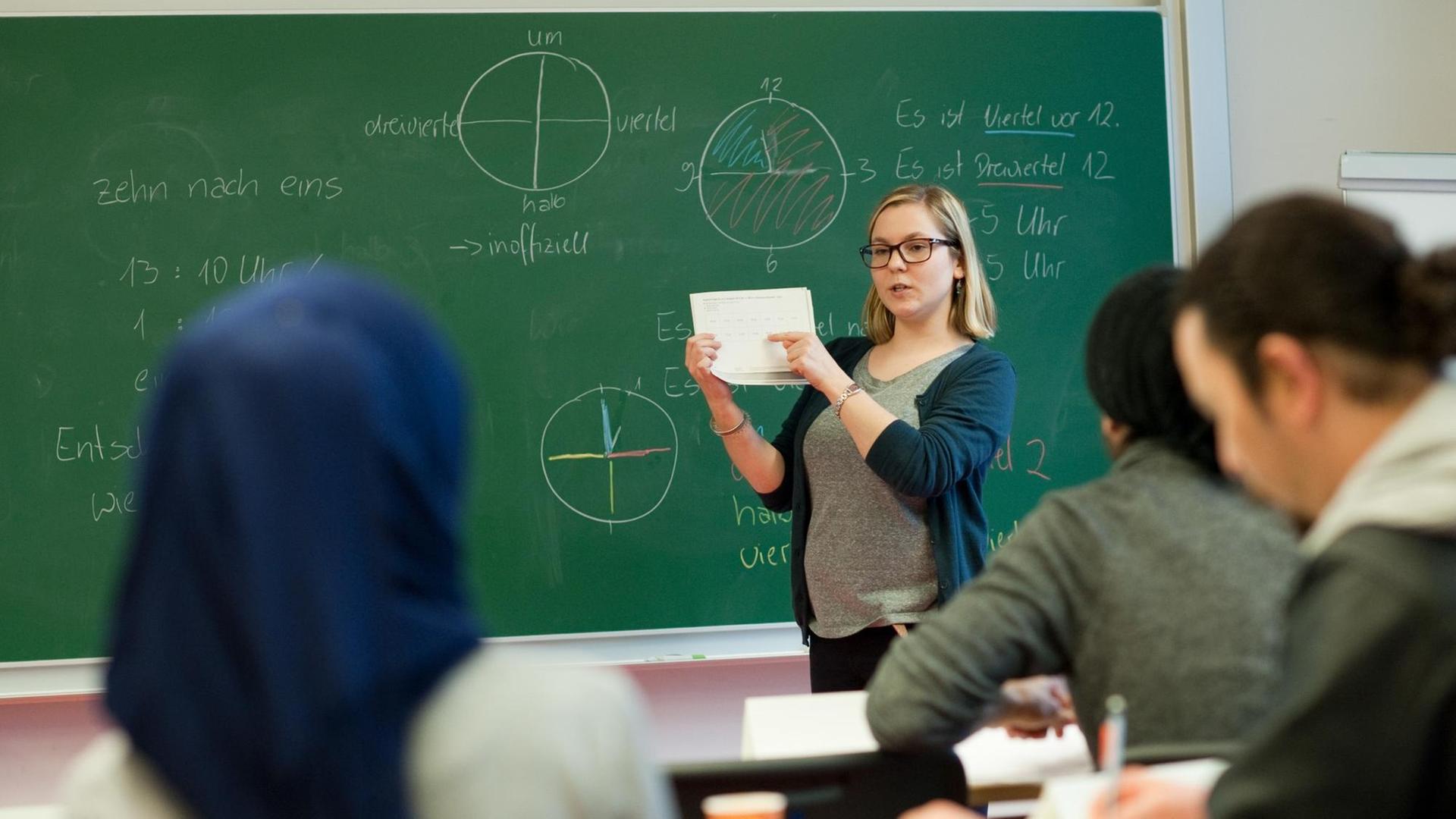 Leiterin des ersten Intensivsprachkurses, Claudia Hubatsch, steht in einem Hörsaal der Uni Potsdam vor einer Tafel vor Schülern und hält ein Blatt Papier in der Hand.