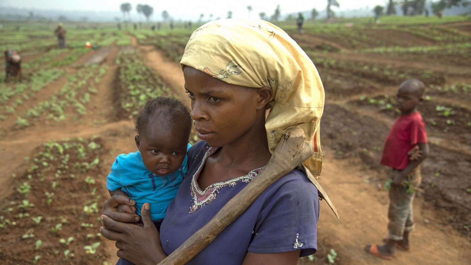 Eine Frau steht mit einem Baby auf dem Arm auf einem Feld in der Demokratischen Republik Kongo