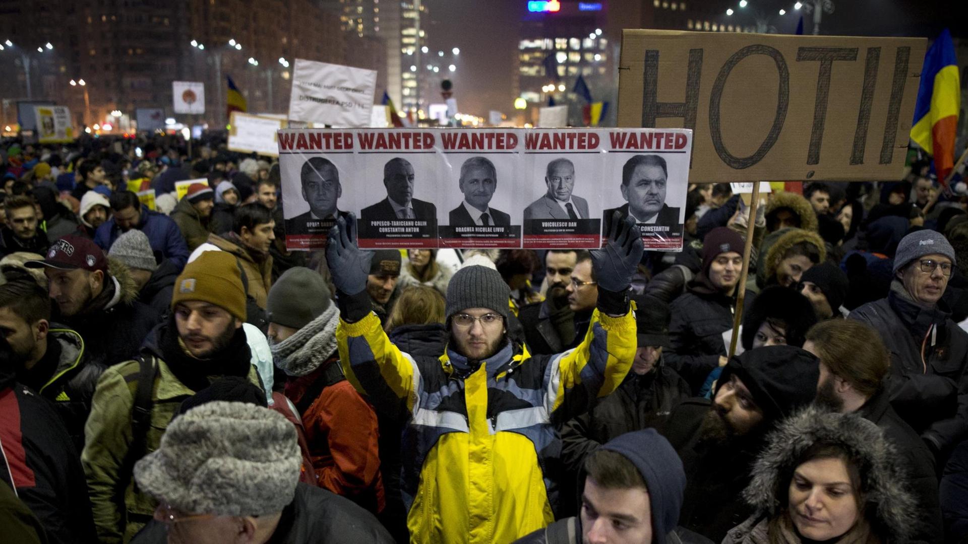 Ein Mann hält in einer Masse von Demonstranten in Bukarest ein Schild hoch, auf dem hochrangige rumänische Politiker mit dem Text "Wanted" zu sehen sind.