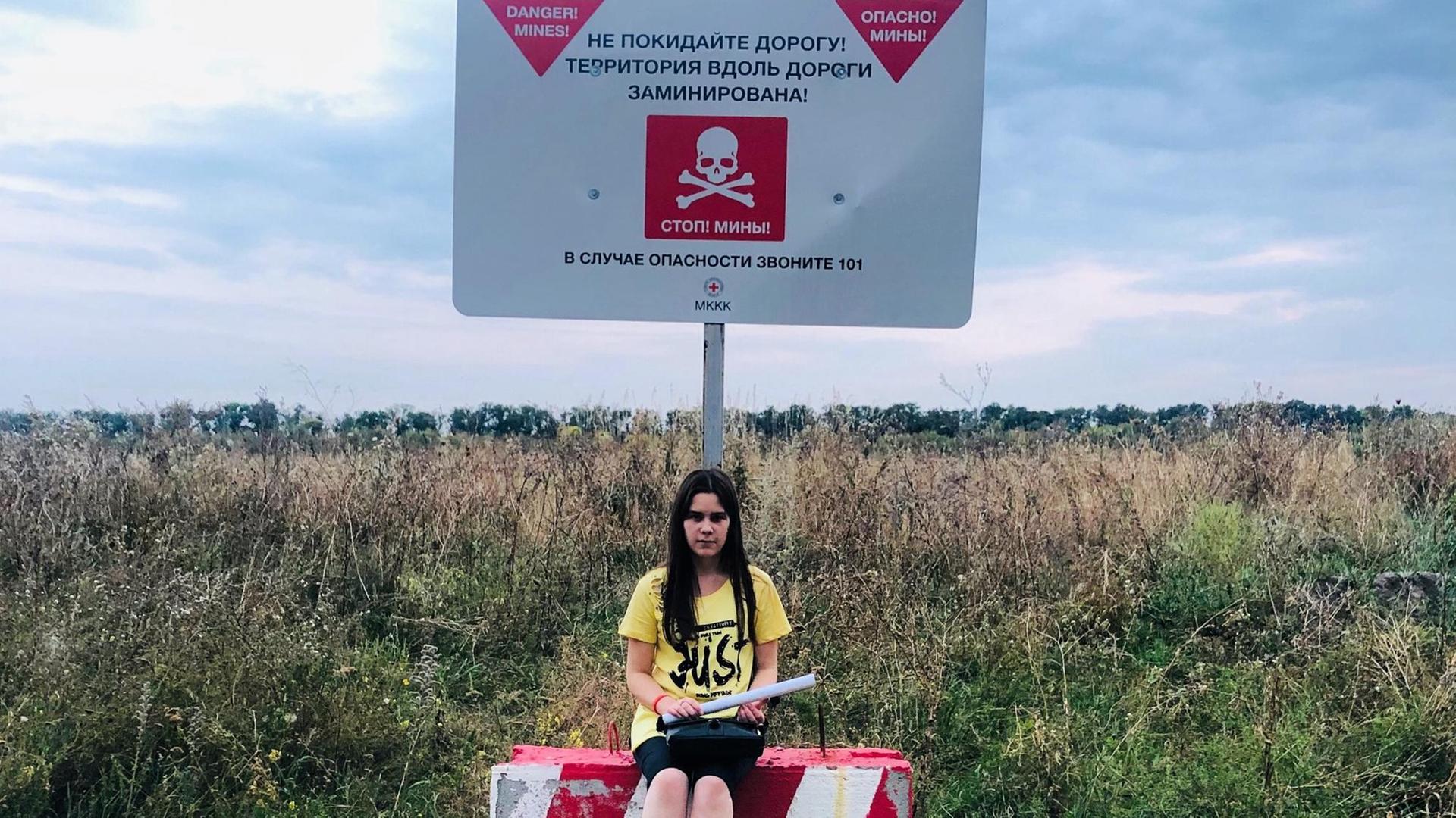 Ein Mädchen sitzt am Rand eines Feldes in der Ukraine.