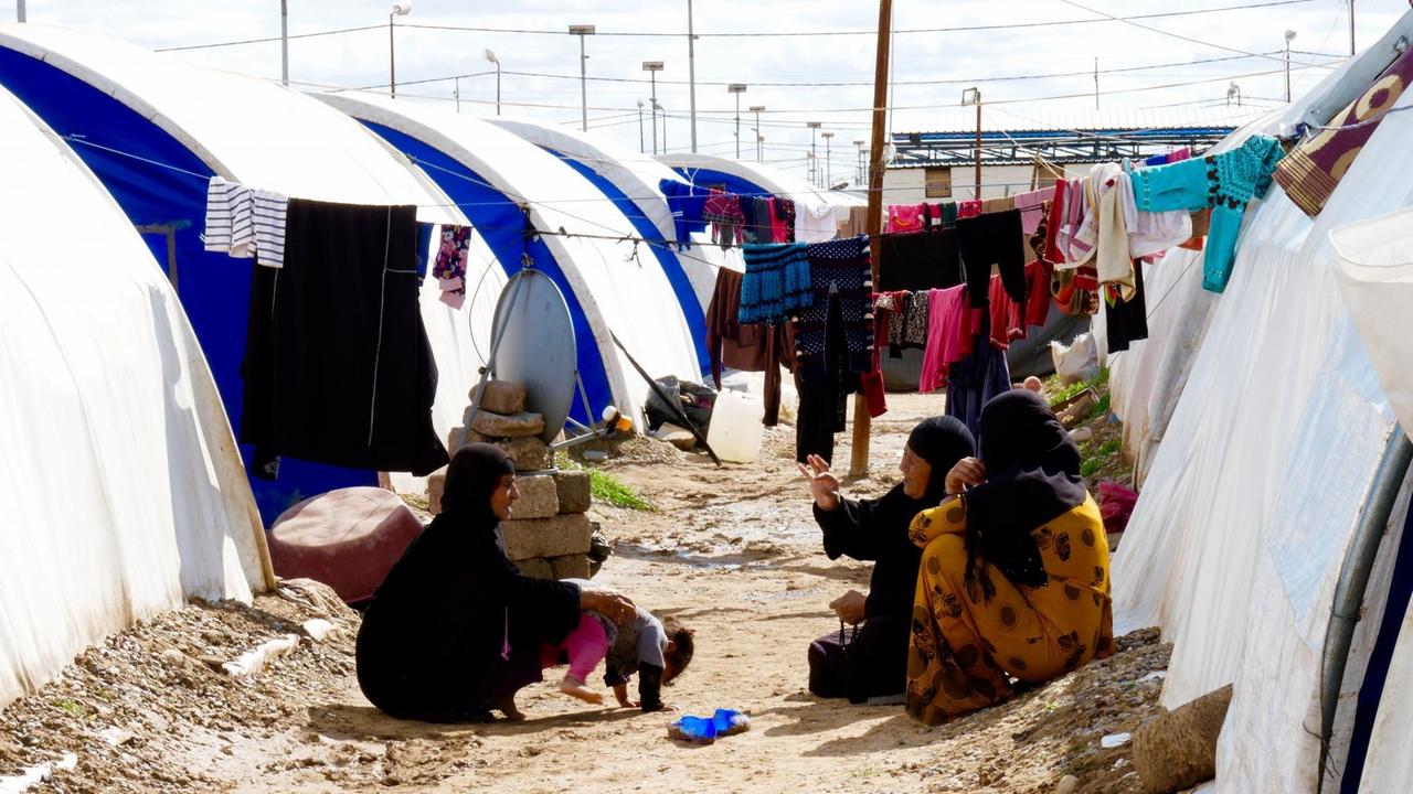 Drei Frauen sitzen zwischen den Zelten im Jadah Lager und unterhalten sich, Kreis Mossul