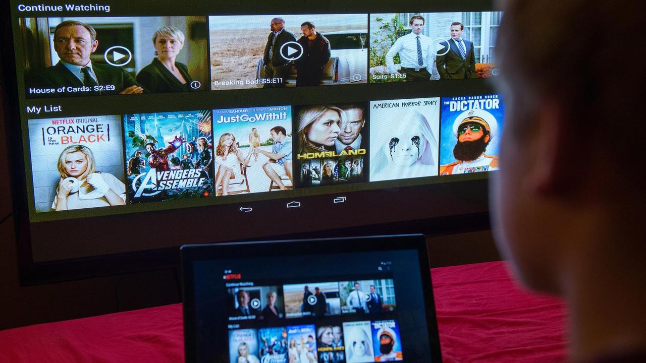 Ein junger Mann lässt sich eine Seite der Videostreaming-Firma Netflix auf einem Laptop und auf einem Fernsehbildschirm zeigen.