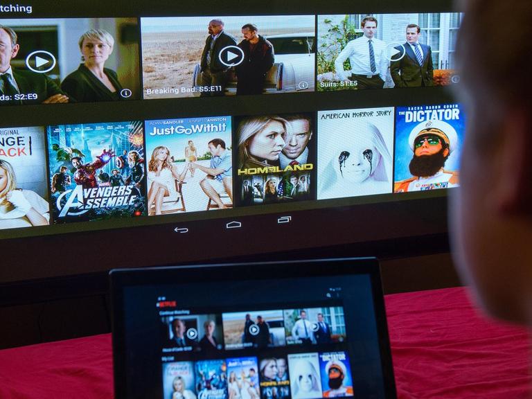 Ein junger Mann lässt sich eine Seite der Videostreaming-Firma Netflix auf einem Laptop und auf einem Fernsehbildschirm zeigen.