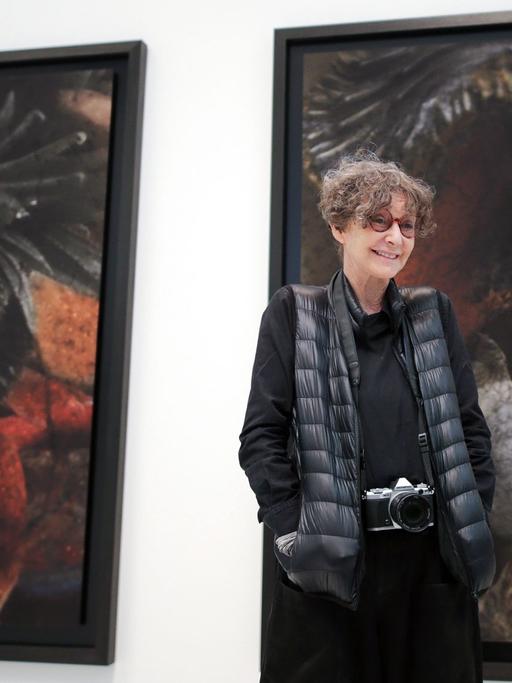 Die französische Fotografin Sarah Moon steht mit einer Kamera um den Hals vor Bildern ihrer Ausstellung in den Deichtorhallen in Hamburg