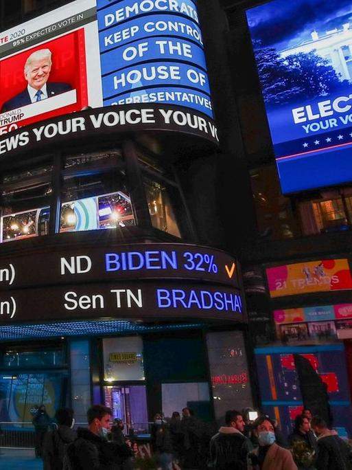 Menschen auf dem Times Square schauen auf riesige Bildschirme, die Donald Trump und Joe Biden sowie die Zahlen der Wahl zeigen.