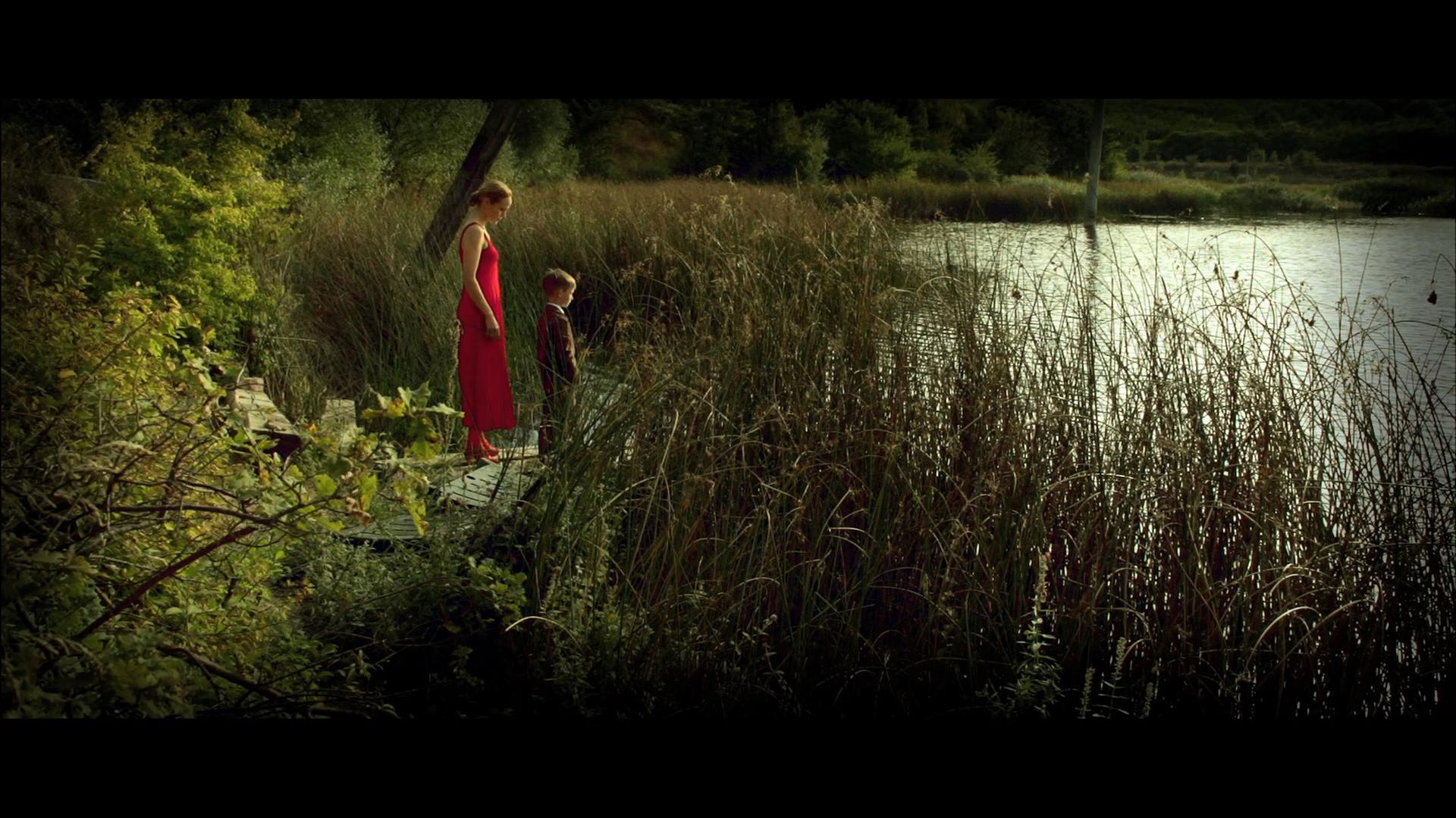 Eine Frau und ein Junge stehen vor einem mit Schilf bewachsenen See.