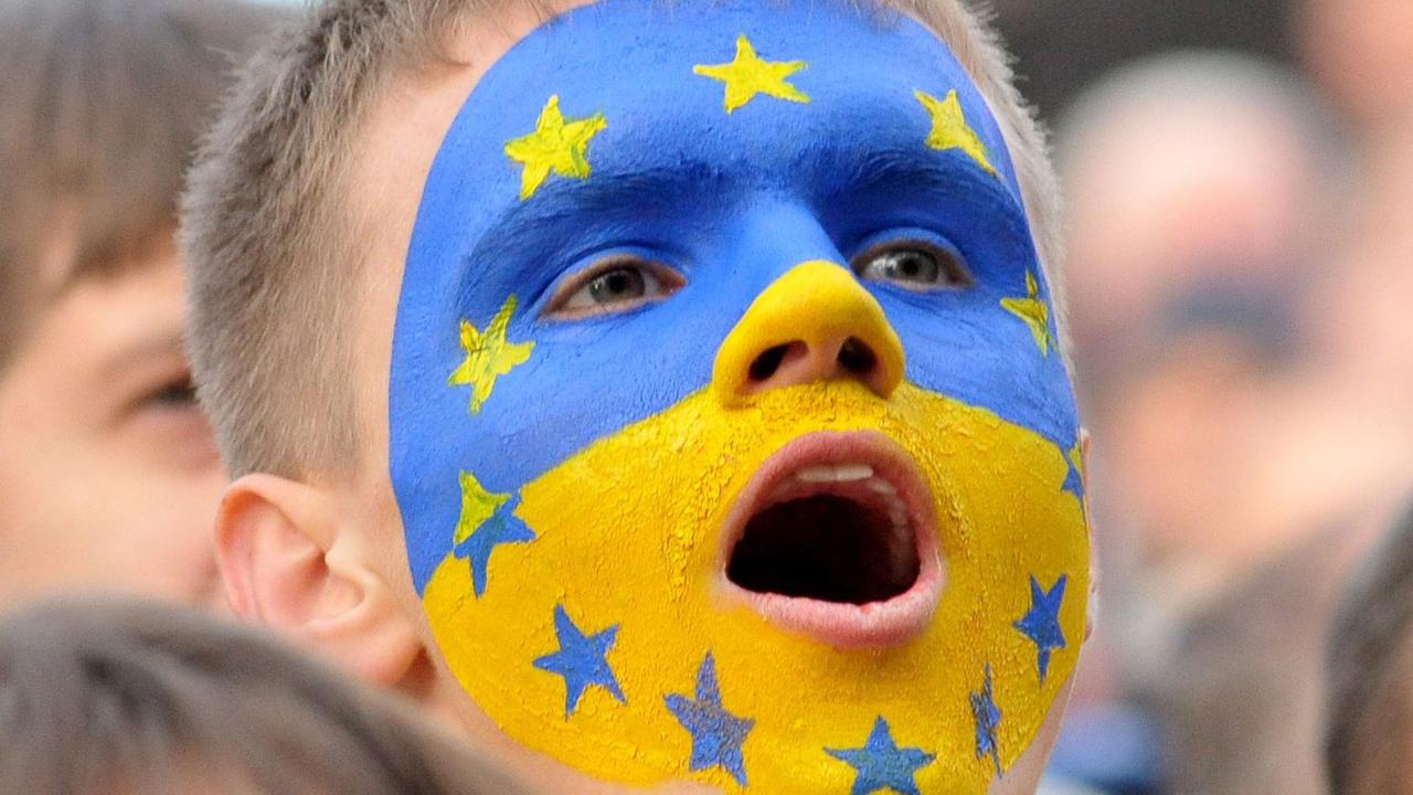Ein Junge mit einer ins Gesicht gemalten gelb-blauen ukrainischen Flagge, auf der auch die Sterne der EU-Fahne zu sehen sind.