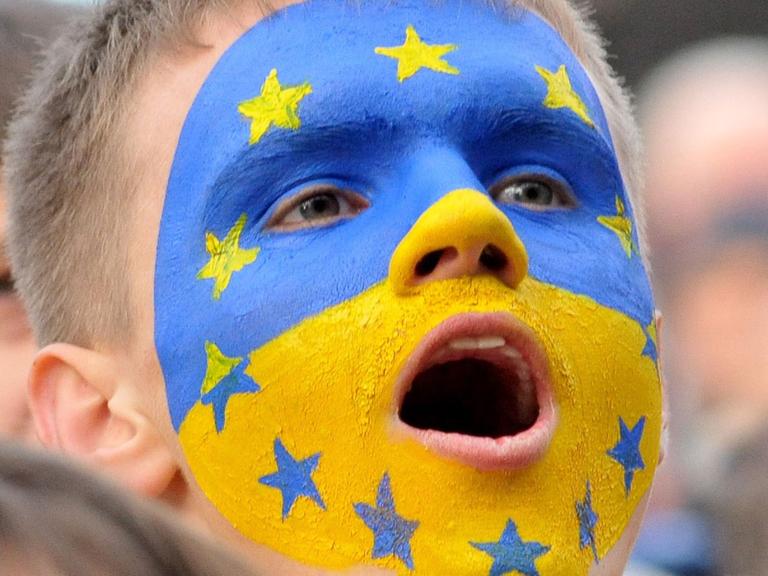 Ein Junge mit einer ins Gesicht gemalten gelb-blauen ukrainischen Flagge, auf der auch die Sterne der EU-Fahne zu sehen sind.