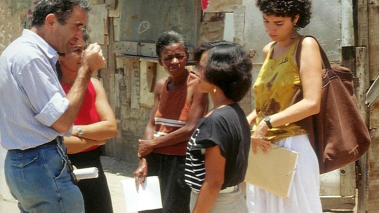 Eine Gruppe Leute steht in einem brasilianischen Elendsviertel und diskutiert mit den Bewohnern.