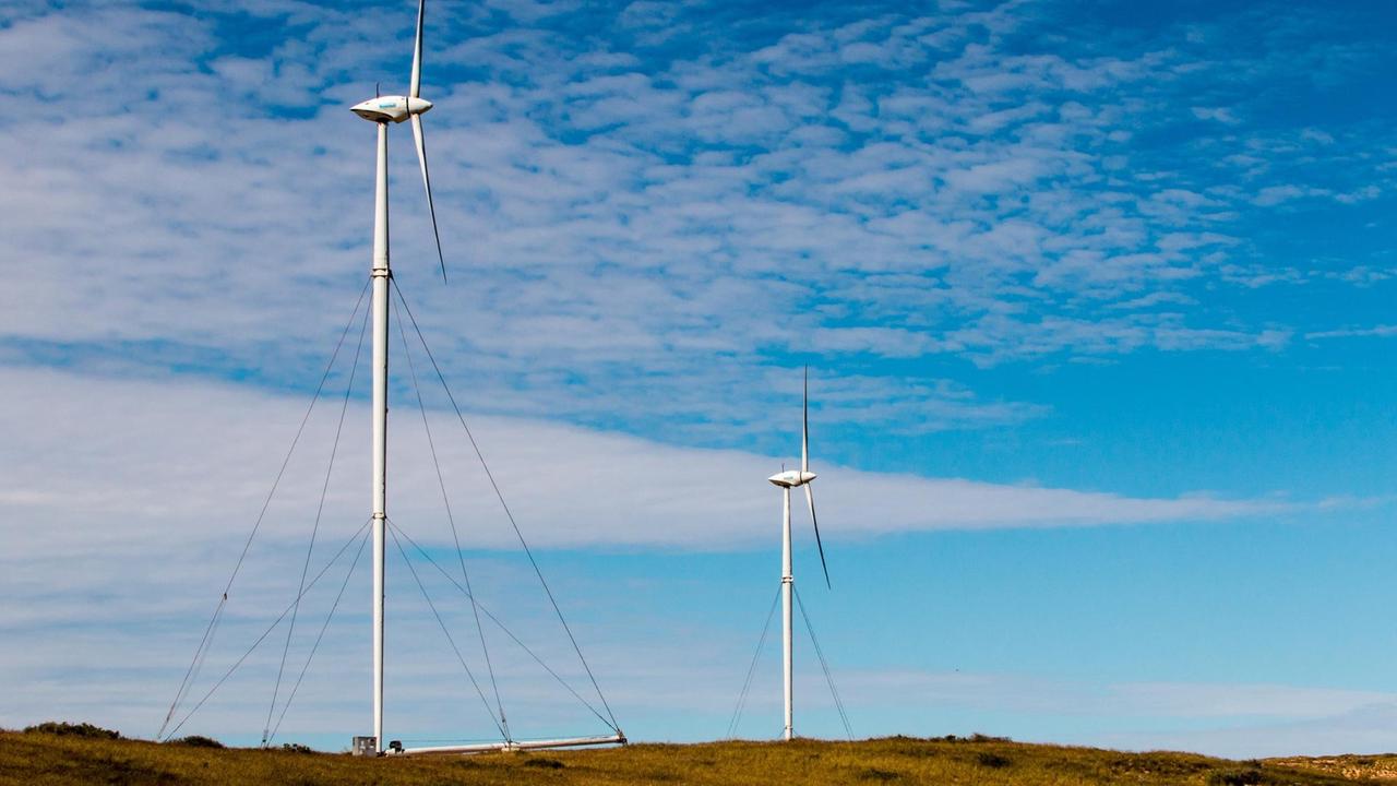 Zwei Windräder stehen in Westaustralien in karger Landschaft vor blauem Himmel.
