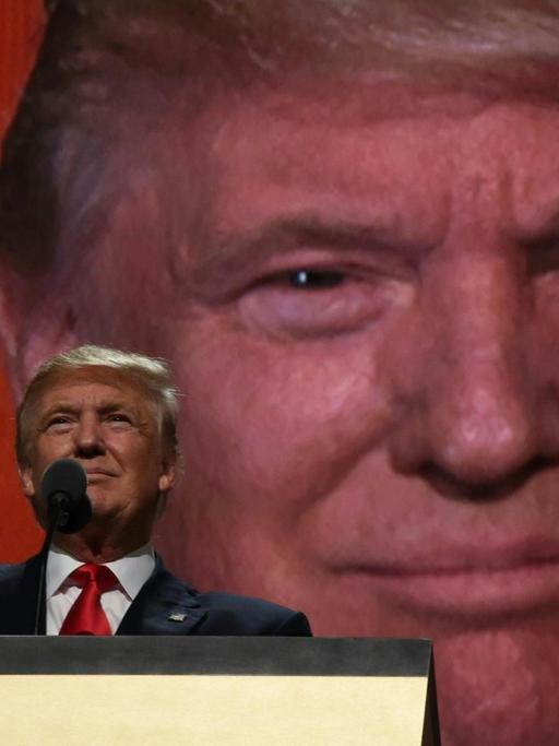 Donald Trump am Rednerpult, hinter ihm sein Gesicht in Großaufnahme auf einer Leinwand