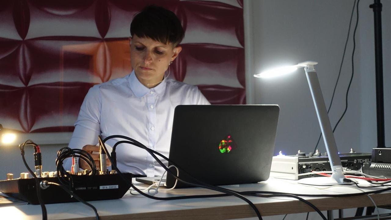 Die Künstlerin Swantje Lichtenstein sitzt bei einer Performance an einem Tisch vor einem Laptop, neben ihr ein Mischpult.