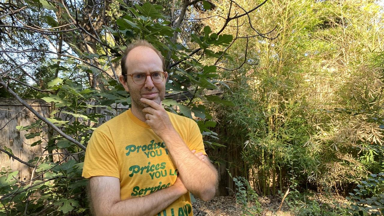 Ein Mann mit lichtem Haar und gelbem T-Shirt steht in einer grünen Landschaft.