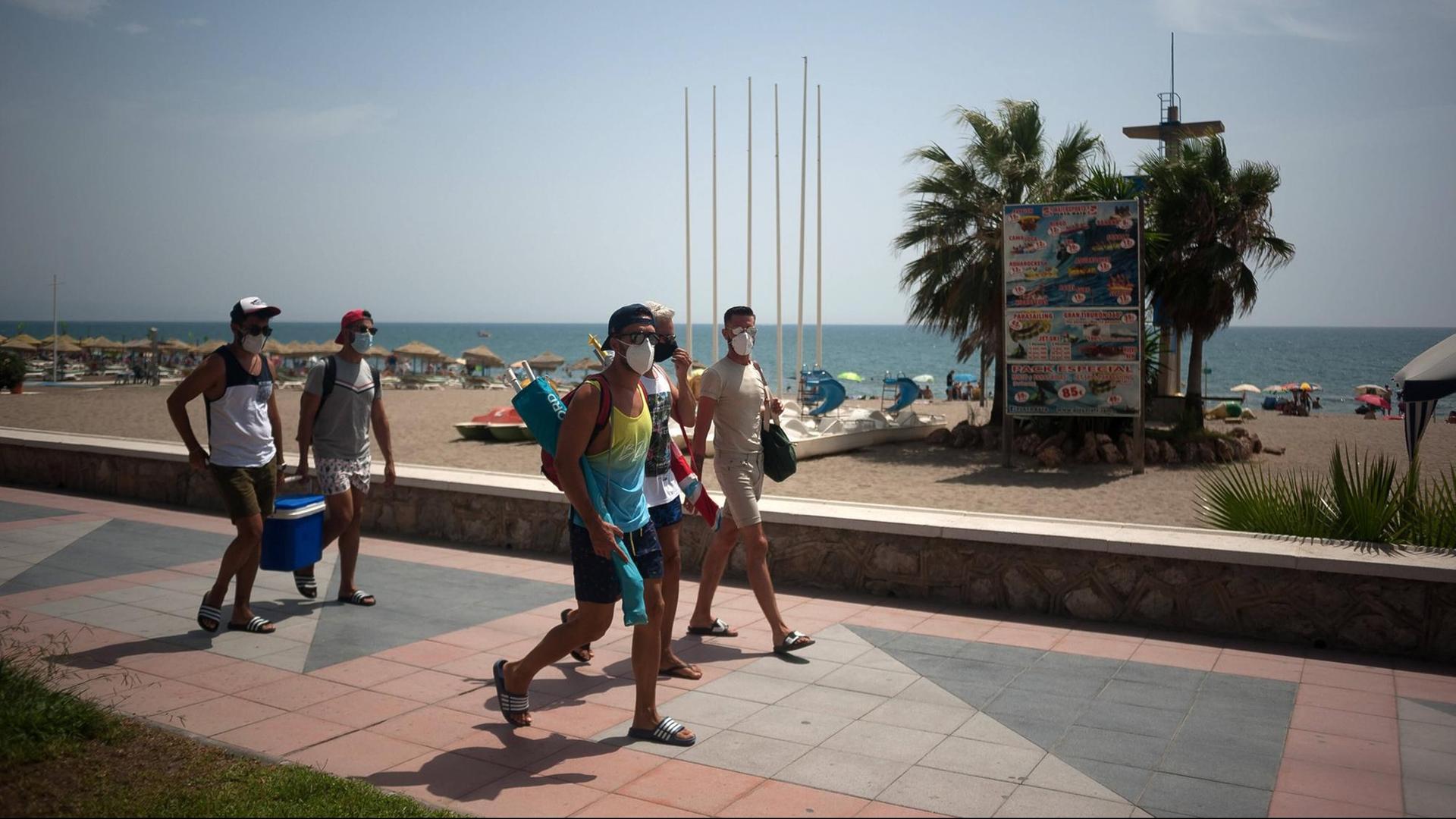 Urlaub in Corona-Zeiten am Strand von Torremolinos in Spanien. Mehrere Menschen laufen mit Mund-Nase-Maske an der Promenade entlang.