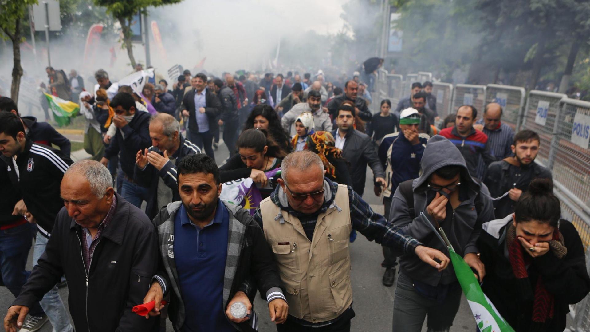 Demonstranten laufen in Richtung des Fotografen, halten den Kopf gesenkt, zum Teil die Hände vors Gesicht, im Hintergrund Tränengas.
