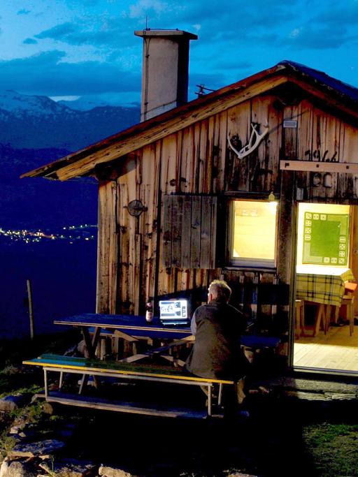Ein Schäfer in Obersaxen in der Schweiz schaut Fernsehen in den Bergen vor seiner Almhütte.