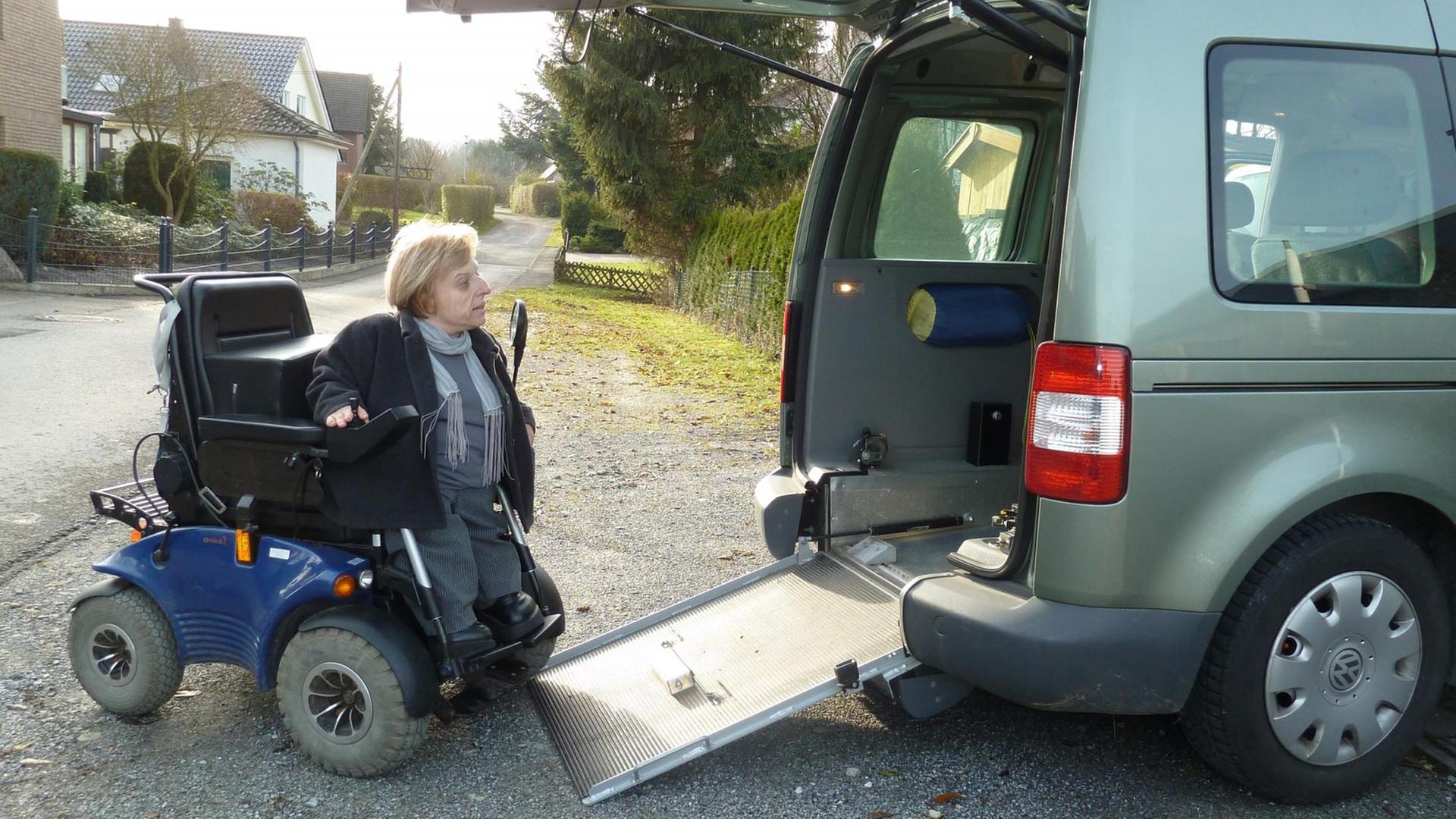 Eine Frau sitzt in einem Rollstuhl und fährt auf einer kleinen Rampe in den hinteren Bereich eines größeren Autos.