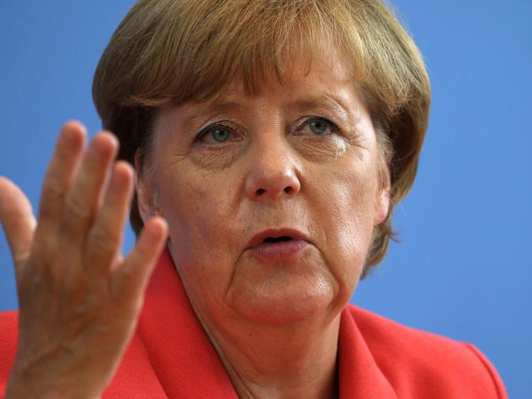 Bundeskanzlerin Angela Merkel in einem rötlichen Jacket gestikuliert mit der rechten Hand.