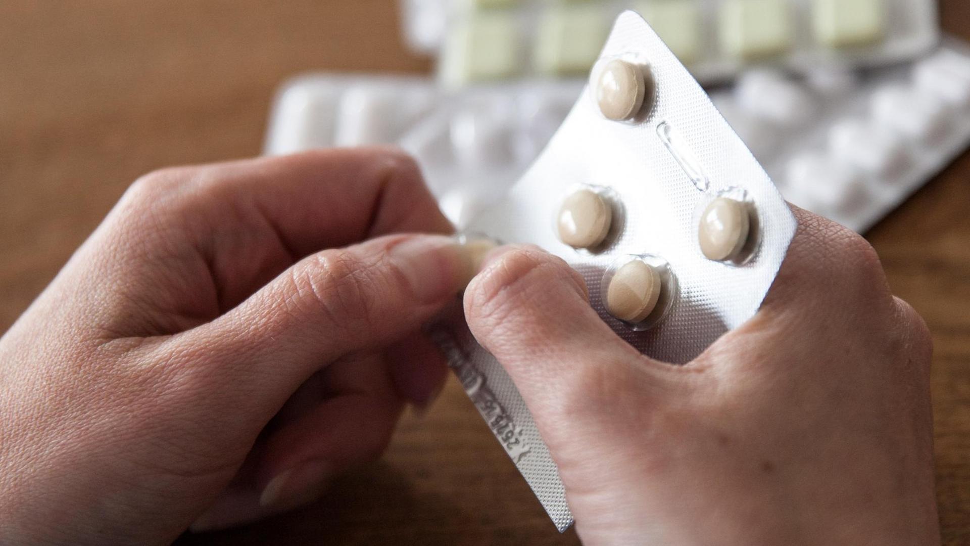 Eine Frau hält Tabletten in ihren Händen, im Hintergrund liegen weitere Blister mit verschiedenen Medikamenten.
