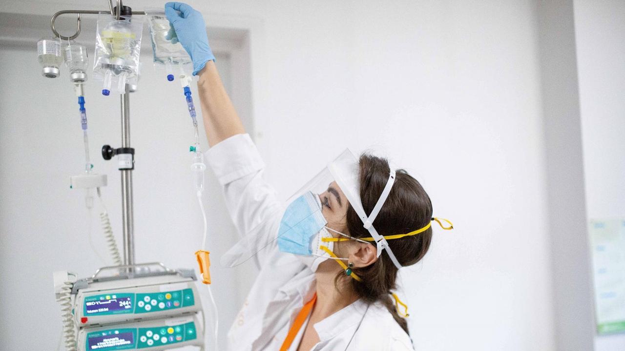 Eine Krankenpflegerin bereitet eine Infusion zur Chemotherapie vor. Sie trägt Mundschutz und ein Kunststoff-Visier