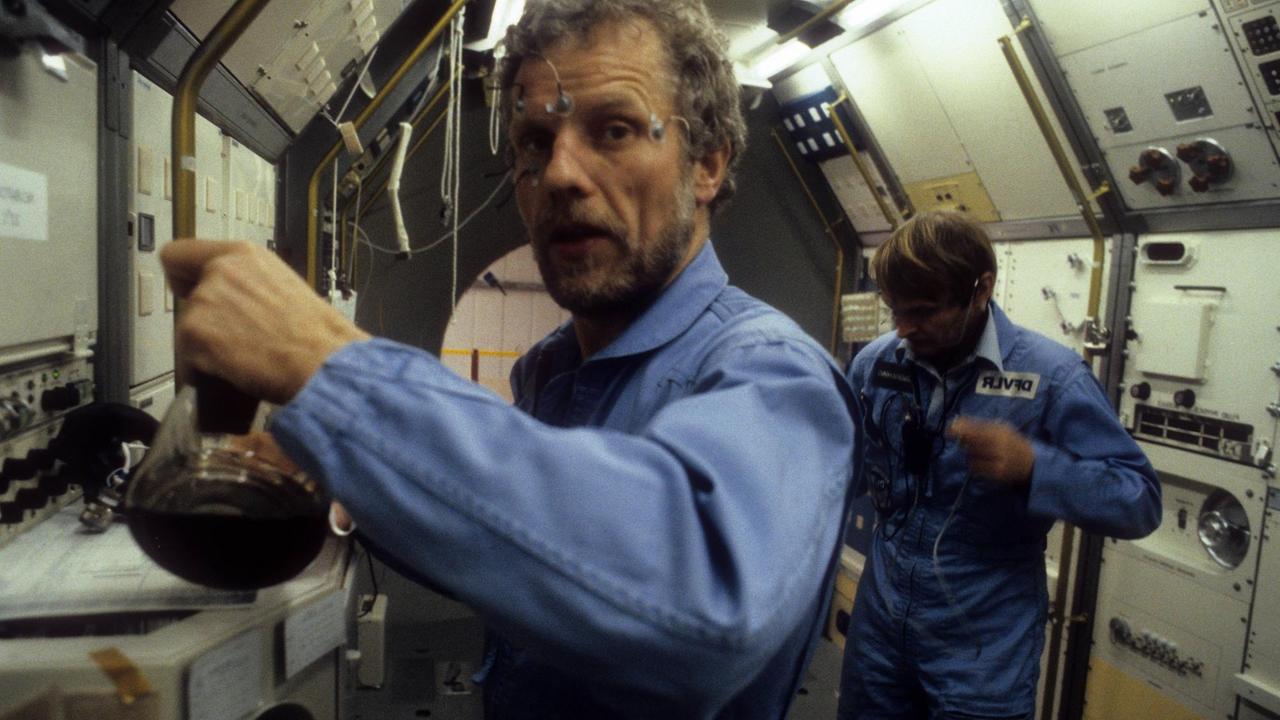 Astronauten Reinhard Furrer und Ernst Messerschmid verkabelt im inneren einer Raumkapsel.