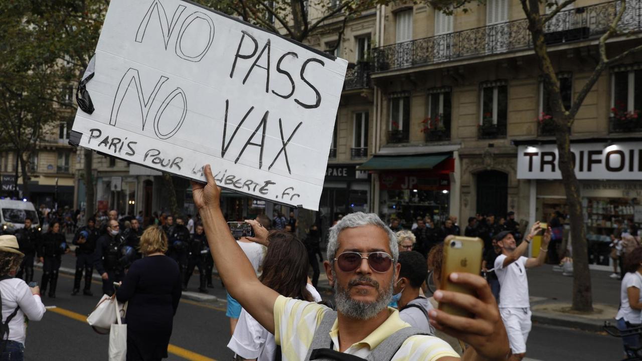 Ein Mann fotografiert sich selbst. Er trägt ein Schild mit der Aufschrift "No Pass, no Vax".