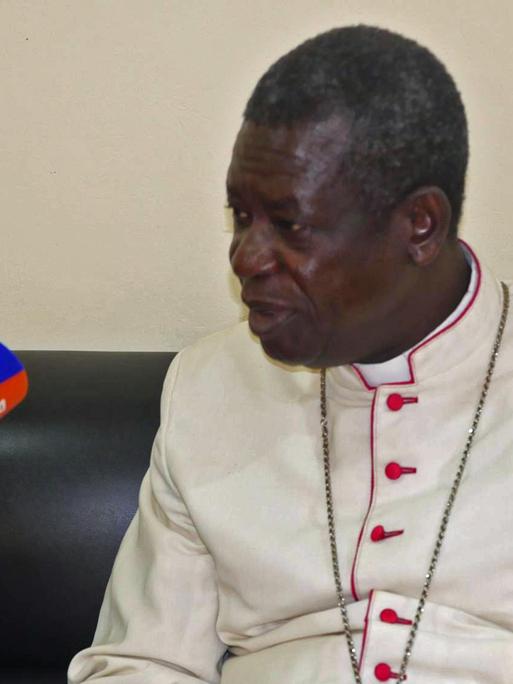 Der Erzbischof von Douala Samuel Kleda sitzt in weißer Soutane auf einer dunkeln Couch beim Interview.