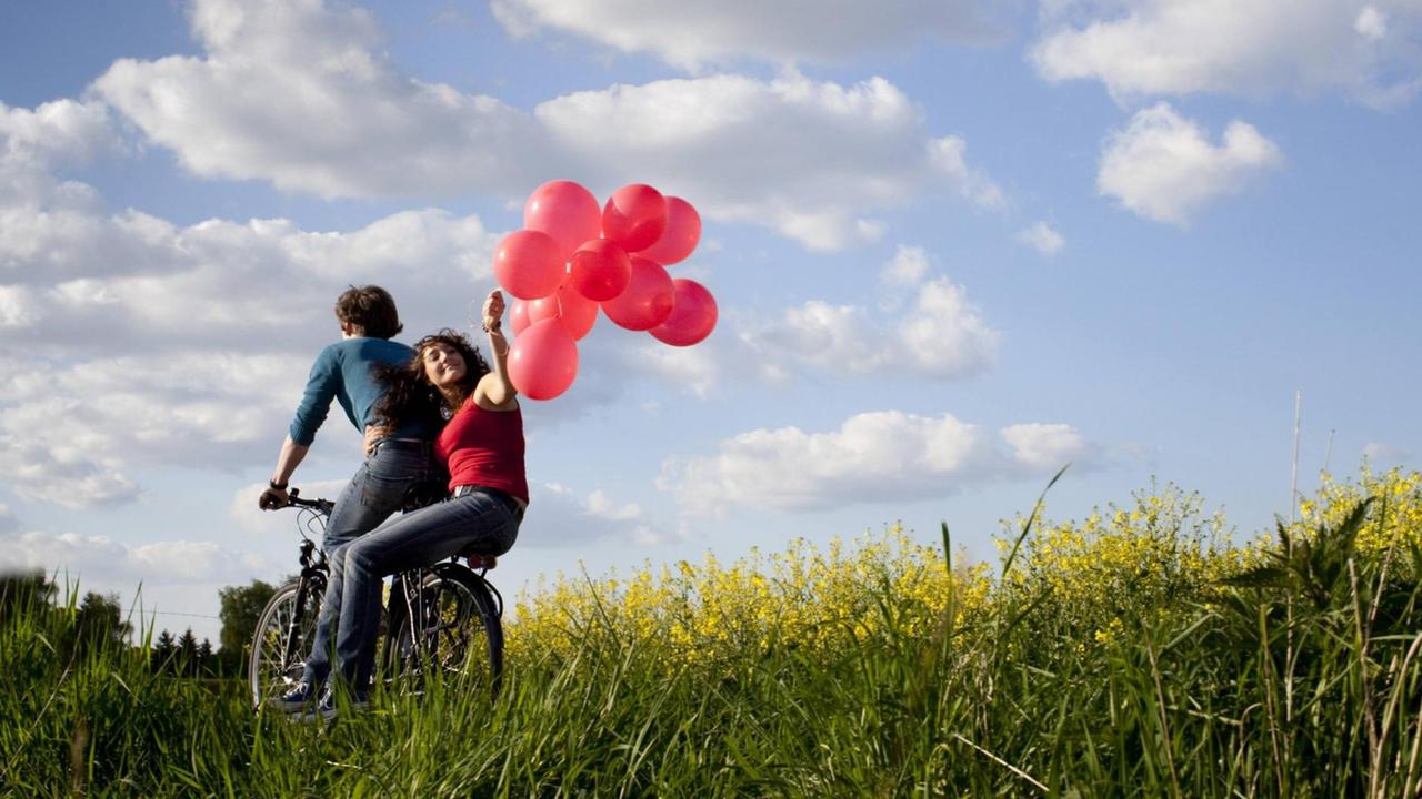 Junges Paar auf einem Fahrrad mit Luftballons