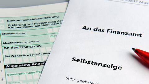 Im Bild ist links ein Steuererklärungsformular und darüber liegend rechts ein weißes Blatt mit dem Titel "Selbstanzeige" zu sehen.