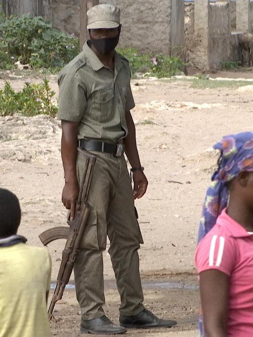 Auf einer Straße steht ein bewaffneter Soldat. Um ihn herum stehen Kinder und Jugendliche.