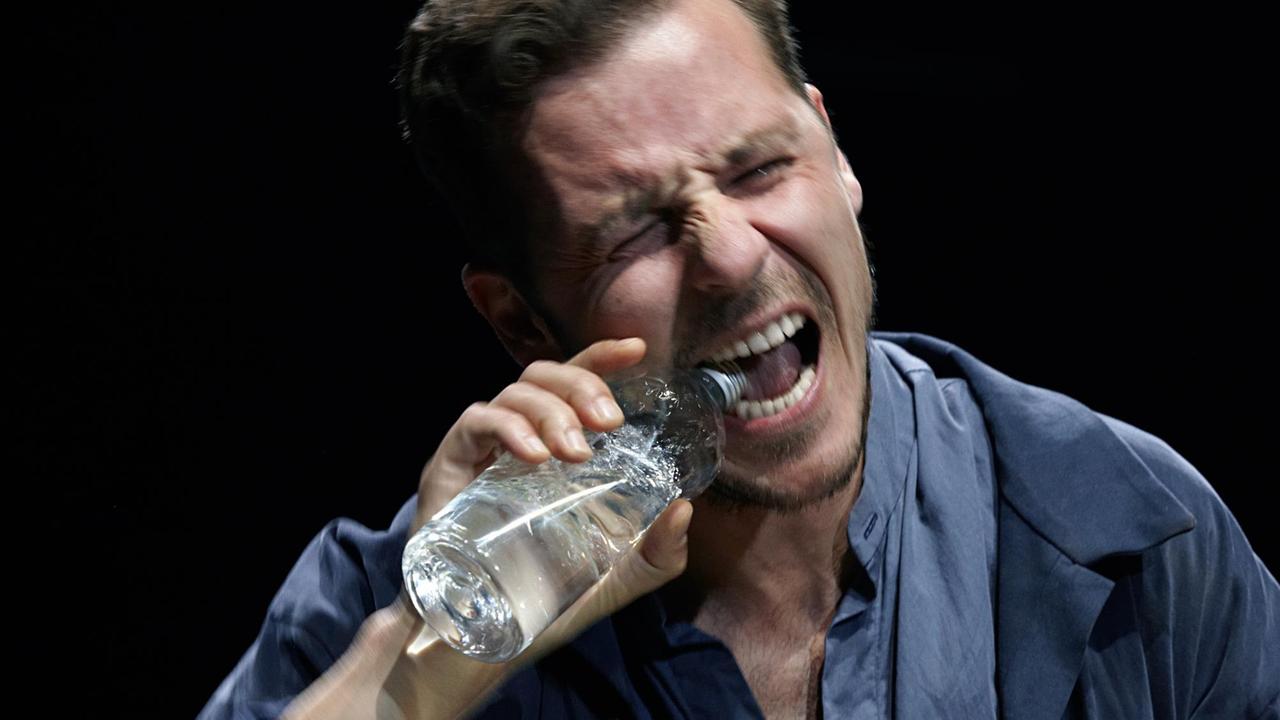 Schauspieler Nils Kahnwald beißt mit von Zorn verzerrtem Gesicht in die Öffnung einer Wasserflasche.