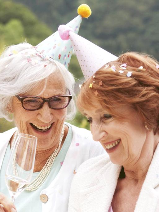 Zwei ältere Frauen trinken auf einer Gartenparty Sekt.