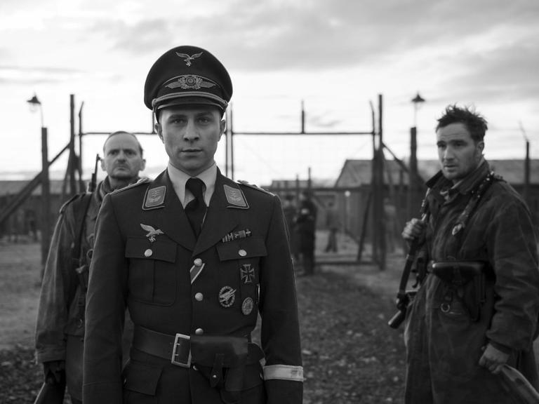 Filmszene aus "Der Hauptmann". Der Hauptmann (Max Hubacher) und die Gefreiten Freytag (Milan Peschel) und Kipinski (Frederick Lau) stehen vor einem Lagertor