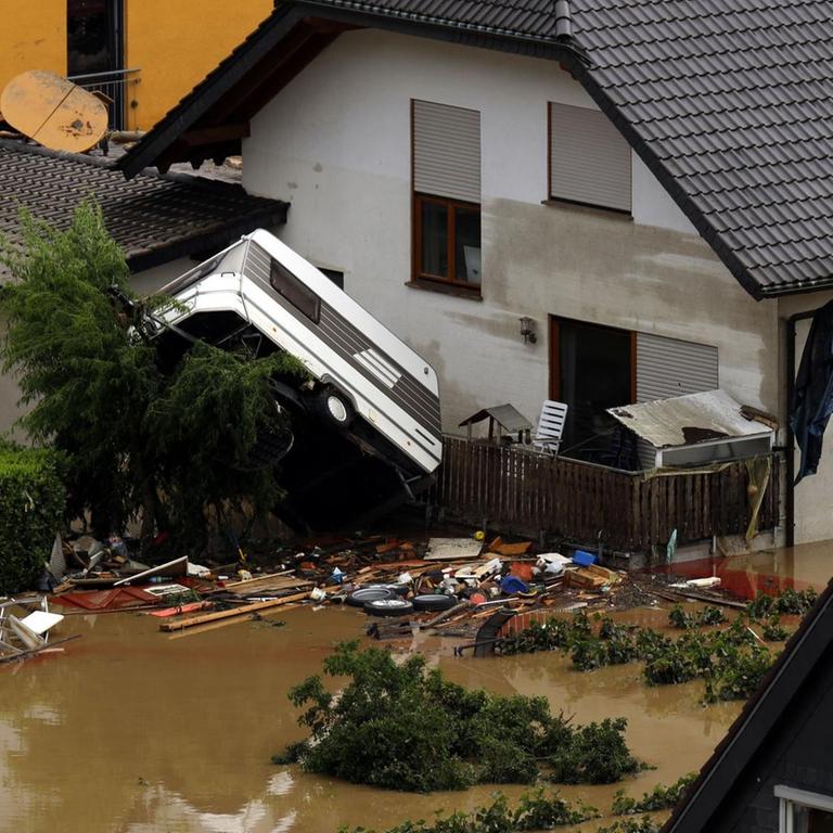 Das Bild zeigt einen überfluteten Garten und einen Wohnwagen, der auf die Terrasse des hauses gespült wurde