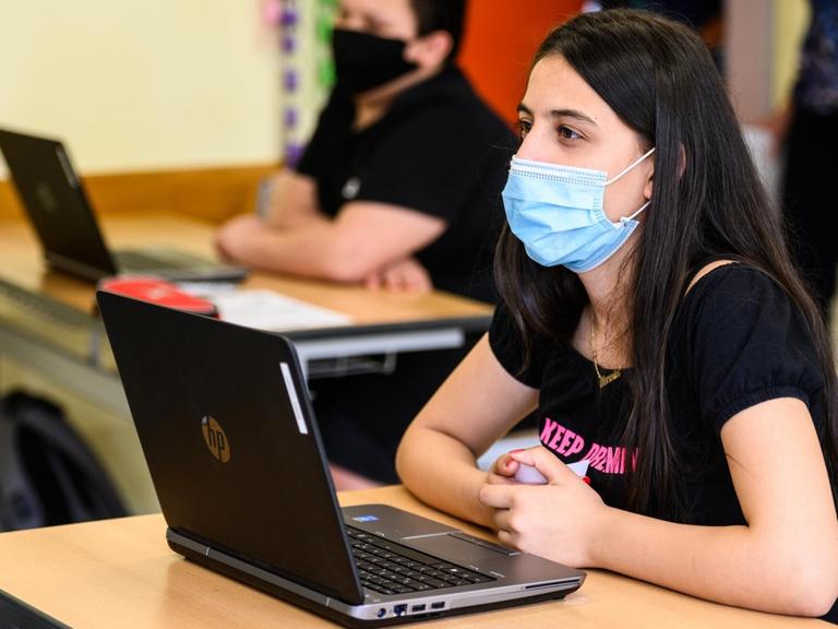 Schülerinnen und Schüler sitzen mit Maske und Laptop im Schulunterricht.