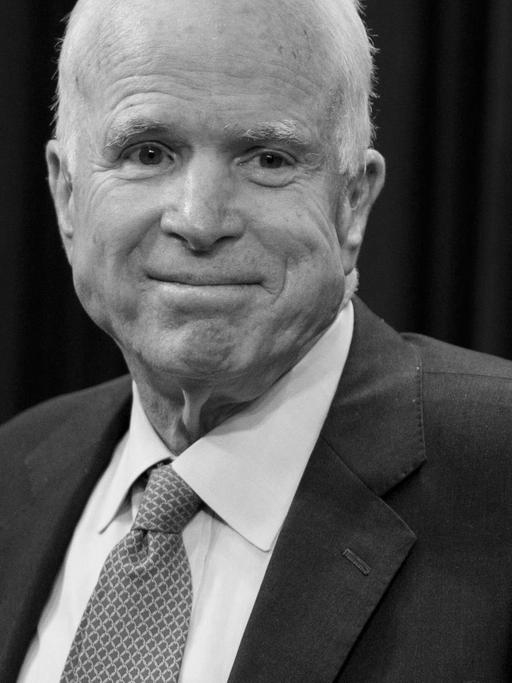McCain steht an einem Rednerpult und lächelt, hinter ihm eine US-Flagge.