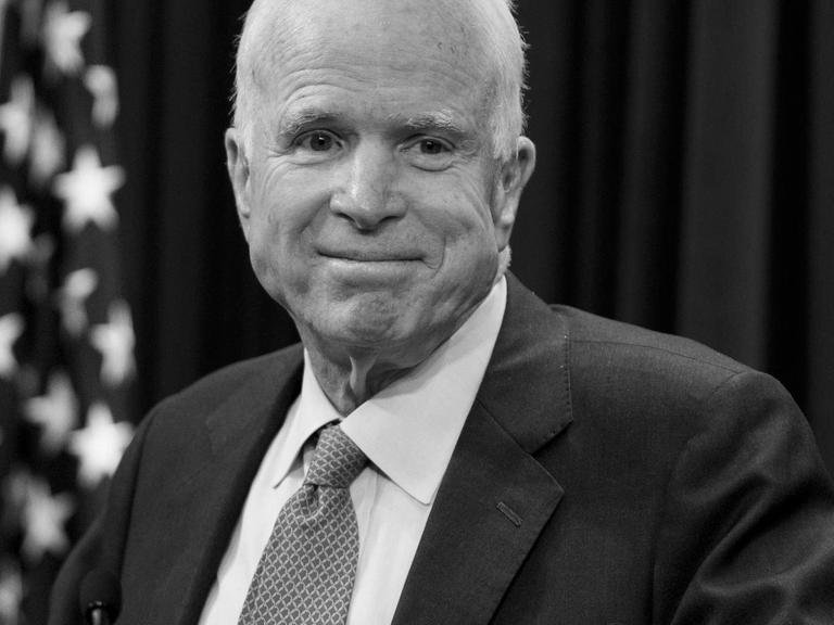 McCain steht an einem Rednerpult und lächelt, hinter ihm eine US-Flagge.